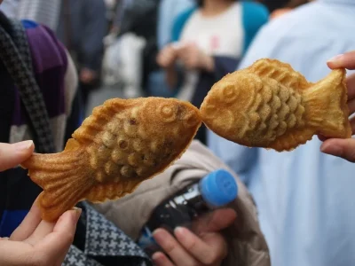 Zwei Personen halten Taiyaki-Waffeln hoch, sodass die Fische aussehen, als würden sie sich küssen