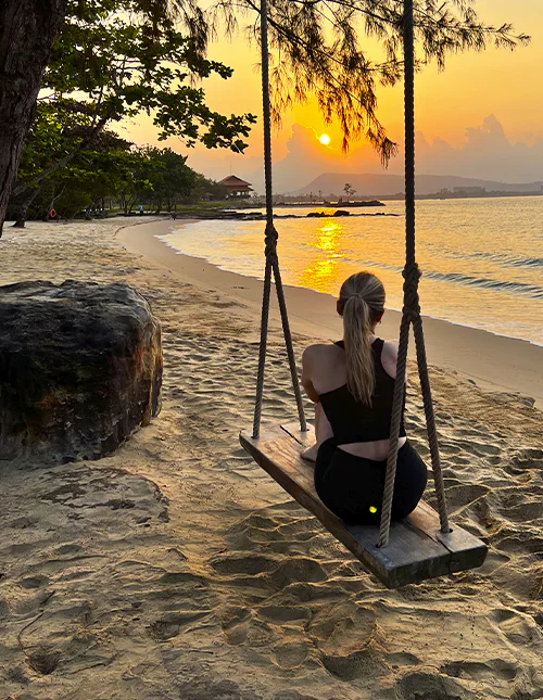 Eine Person sitzt auf einer Schaukel am Strand und genießt den Sonnenuntergang