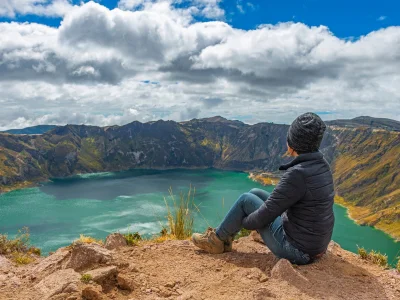 Eine Frau sitzt am Rand des Quilotoa-Kratersees in Ecuador.
