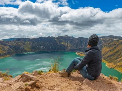 Eine Frau sitzt am Rand des Quilotoa-Kratersees in Ecuador.