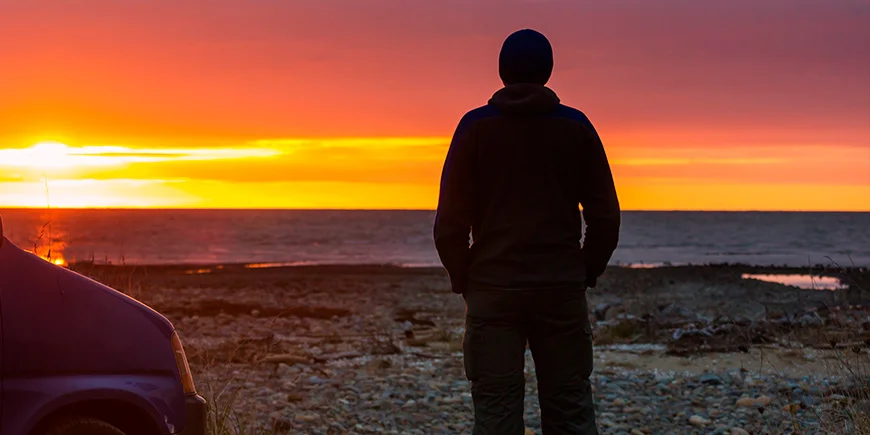 Mann genießt Sonnenuntergang am Wasser in Neuseeland