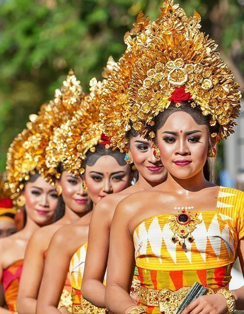 Traditionelle balinesische Tänzerinnen und Tänzer in farbenfrohen Kostümen und mit goldenem Kopfschmuck in einer Prozession.