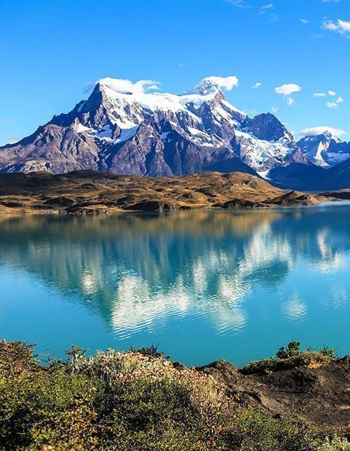 Ein Bergsee, in dessen türkisfarbenem Wasser sich schneebedeckte Gipfel unter einem wolkenlosen Himmel spiegeln.